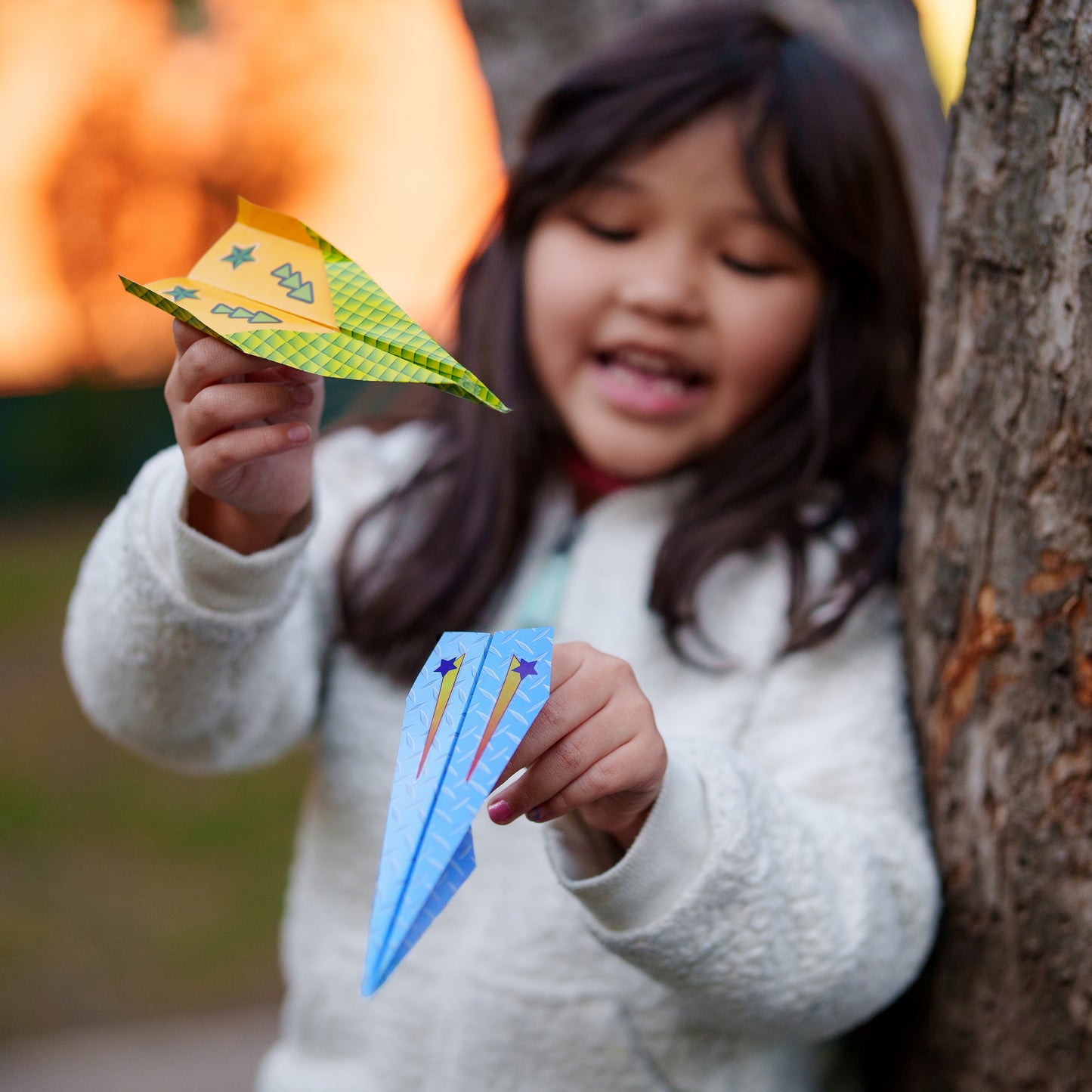 Child holding two paper airplanes against a natural background