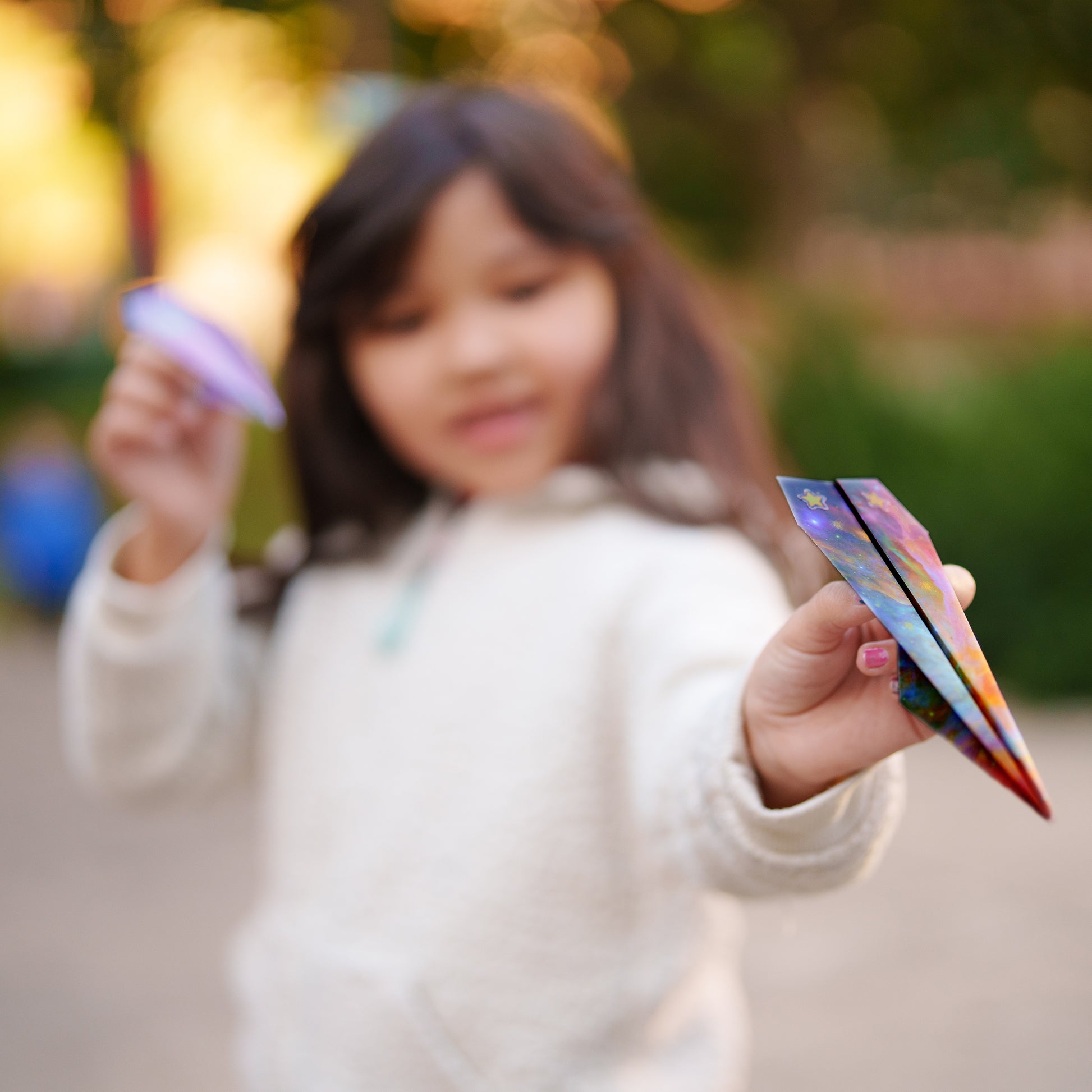 Child flying a handmade paper airplane during outdoor play