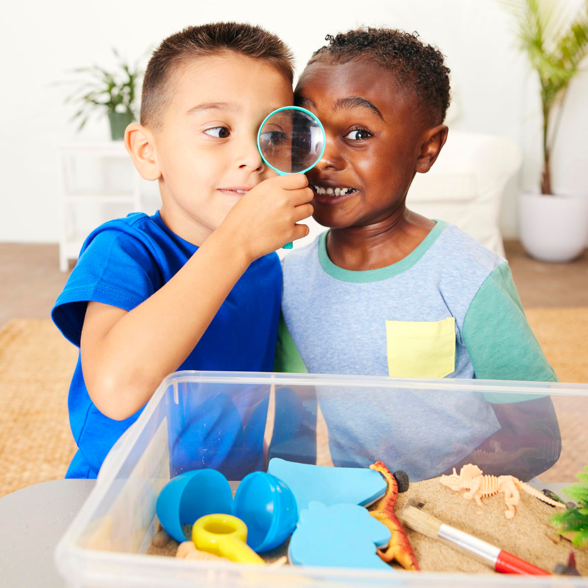 Children exploring and playing with the Creativity for Kids Dinosaur Sensory Bin using a magnifying glass