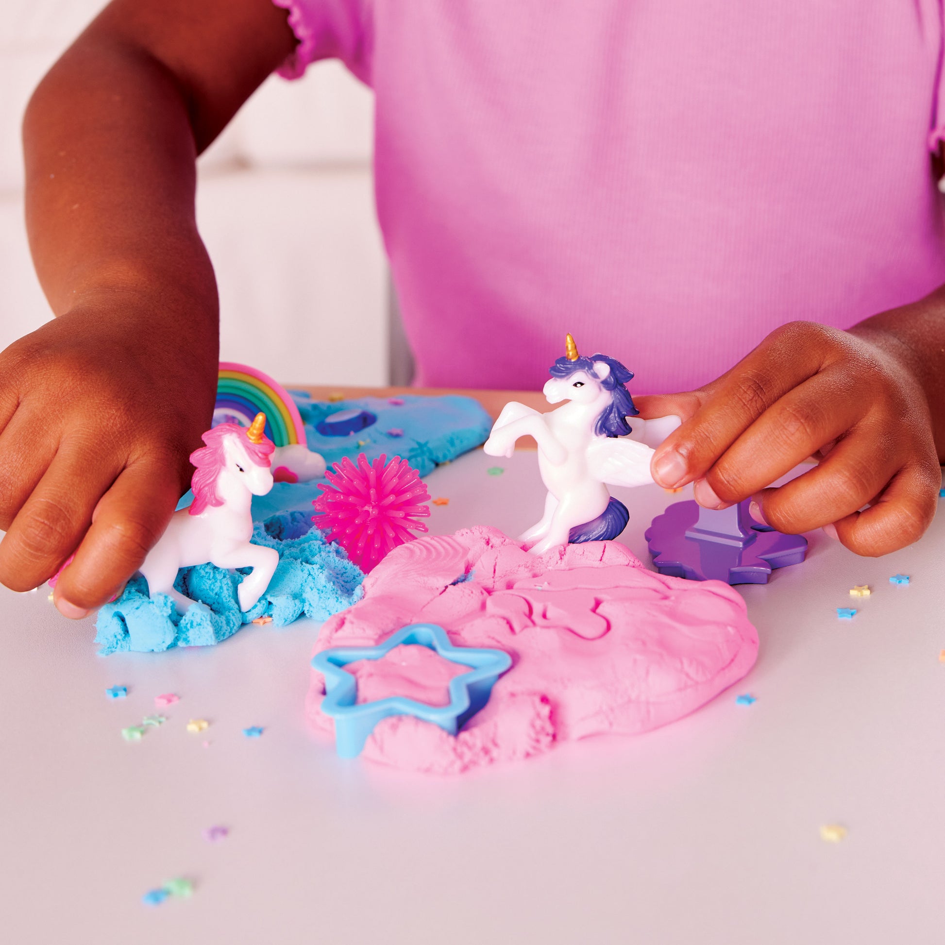 Hands playing with unicorn figures and colourful stretchy cloud clay